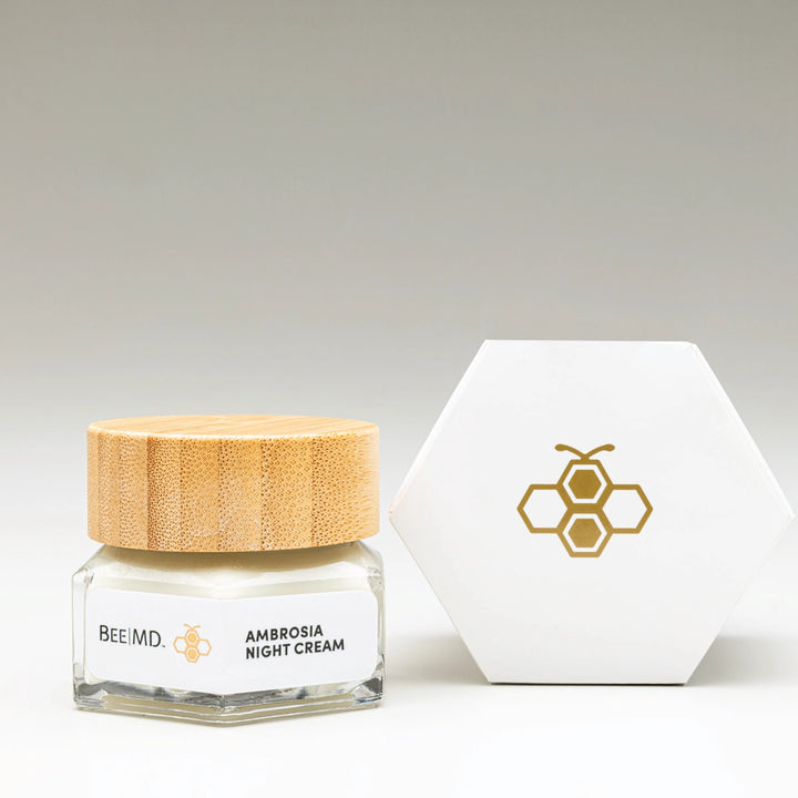 BEEMD Ambrosia Night Cream in glass jar with wooden cap next to hexagonal packaging, displayed on a minimal light background.
